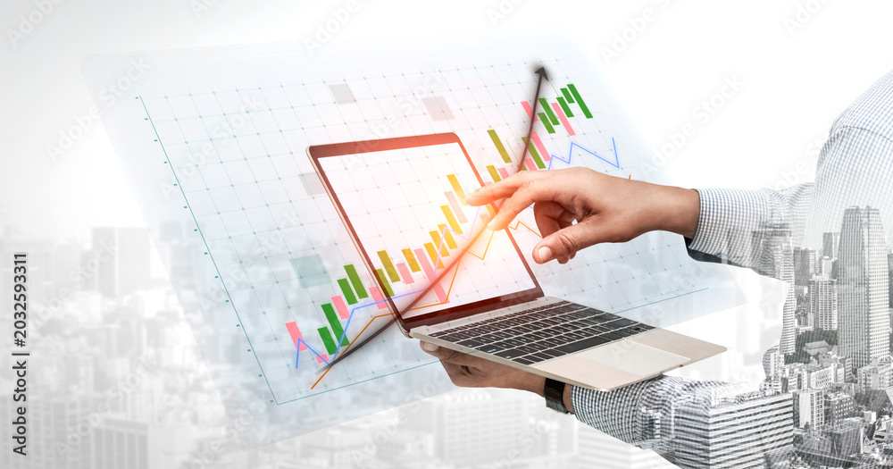 Obraz premium A hand interacts with a laptop displaying a vibrant data chart overlay, symbolizing the fusion of technology and finance in a busy urban setting. Impute
