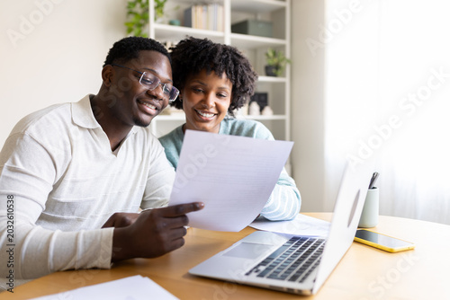 Happy couple reading documents and working on laptop at home