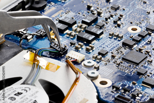 Obraz na plátně Laptop motherboard repair with tweezers and cooling fan close up