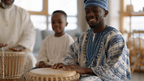 Nigerian father in traditional embroidered kaftan teaching young son drumming patterns on authentic hand drum in apartment living room while elder uncle demonstrates proper technique during weekend 