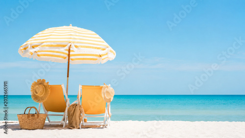 Yellow beach chairs and striped umbrella set on white sand with beach accessories beautiful tropical seaside landscape under blue sky wide landscape photograph