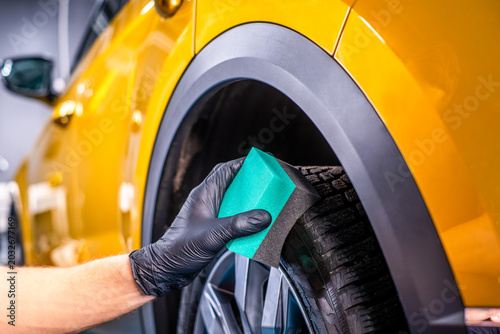 Hand cleaning car tire with green sponge, deep cleaning and exterior car wash concept
