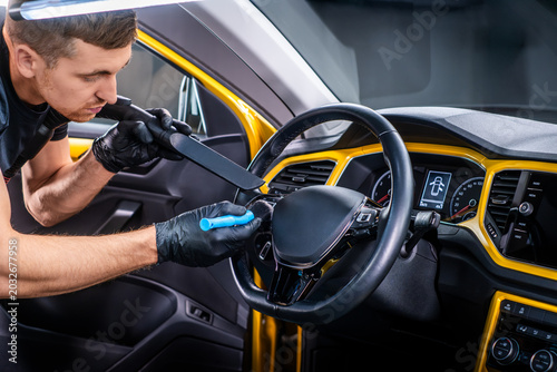 Man cleaning car steering wheel with brush and vacuum cleaner, interior car wash detailing and vehicle care concept
