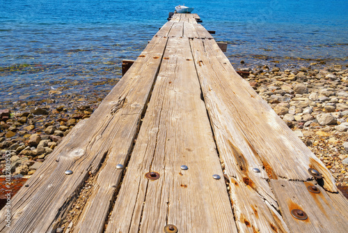 Old wooden jetty leading to small white boat. Perspective view
