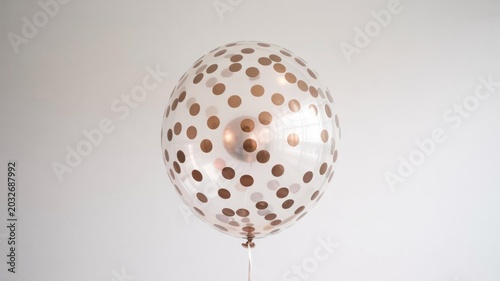 Shiny white balloon with gold polka dots floats freely on a plain background for party decoration