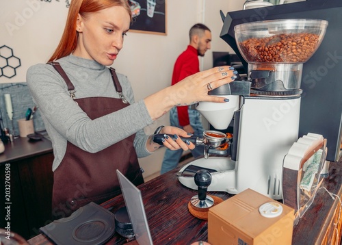 young woman preparing ground coffee with professional grinder in cozy cafe interior while working behind counter. coffee culture, small business and barista profession concept