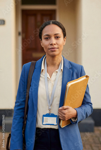 Black Social Worker with Folder and ID Badge Standing at House Door