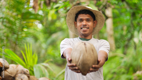 Portrait of smiling young indonesian farmer with harvested coconut for copra on farm on flores island, indonesia, southeast asia, straw hat