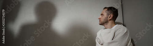 Foto Website header shot of Caucasian young man sitting in restraint garment and looking away beside shadow, conveying mental health crisis, isolation, psychiatric care