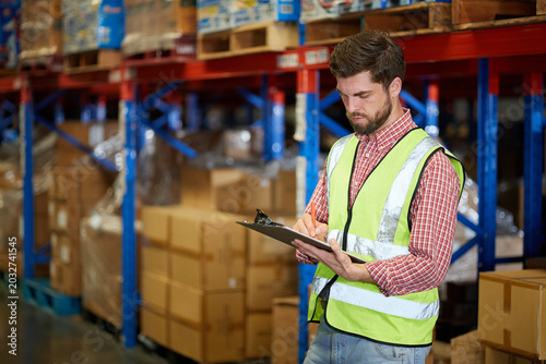 Workers diligently taking notes on a a clipboard in a large warehouse