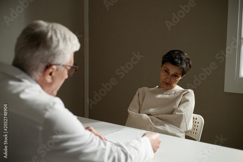 Cuadro en lienzo Middle aged woman sitting restrained during psychiatric evaluation, listening to senior male doctor, conveying mental health crisis and treatment