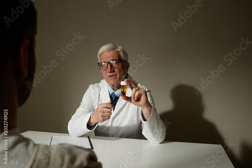 Fotografija Senior Caucasian male doctor holding prescription bottle, explaining medication