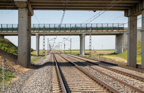 Railway Tracks Under Concrete Overpass With Electric Lines Through Open Rural Landscape
