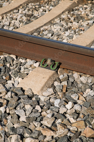 A close-up view of a railway track showing a concrete sleeper, steel rail, green metal fastener and crushed stone ballast, highlighting industrial textures, construction detail and transportation infr