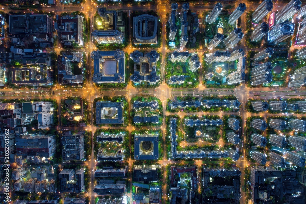 Fototapeta premium Overhead Aerial Night View of a Gridlike Cityscape Illuminated by Golden Streetlights and Building Lights Showing Dense Urban Development and Traffic Flow