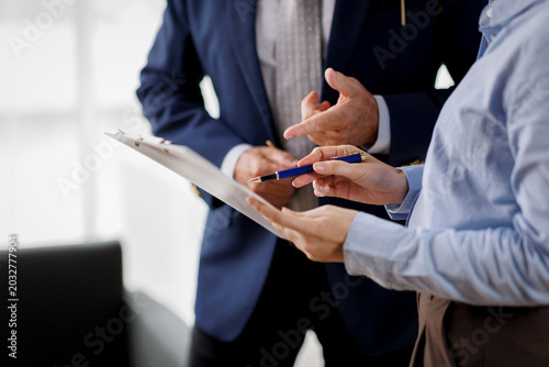 Corporate Business Colleagues Discussing Financial Report on Clipboard, Female Employee Showing Data to Male Executive Manager in Suit during Professional Briefing or Meeting in Bright Office