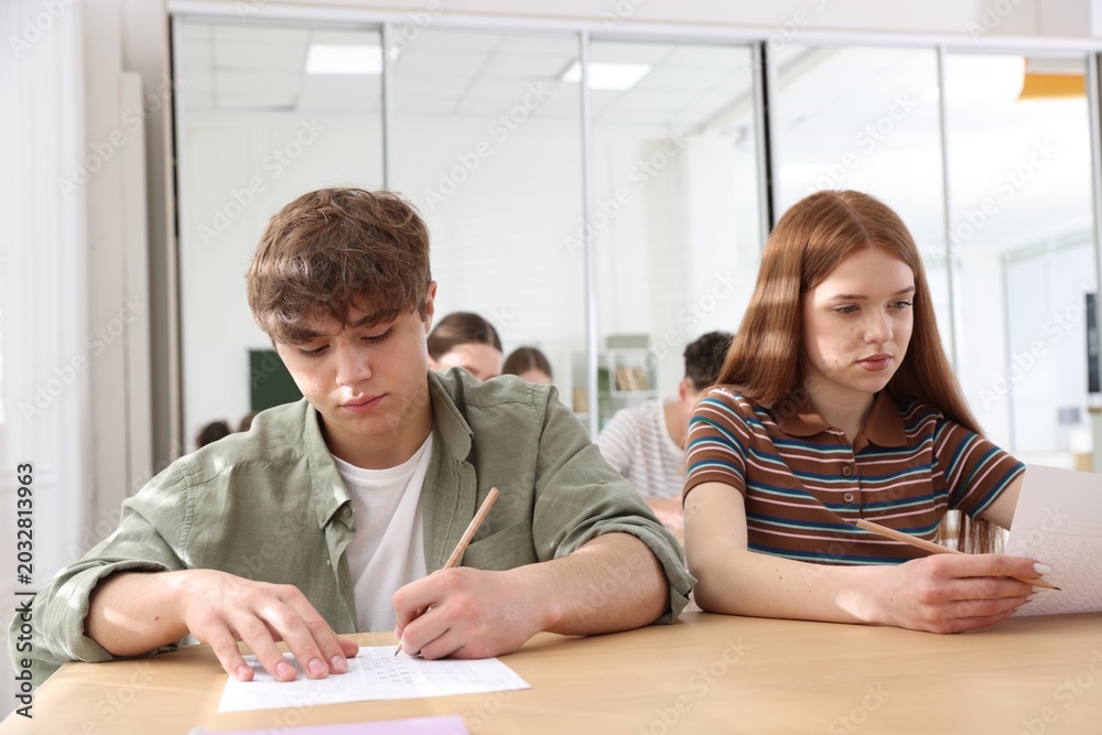 Fototapeta premium Group of students taking test at wooden desks in classroom