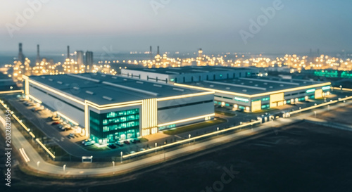 Blurred abstract background of a modern industrial warehouse building and logistics distribution center at night with glowing architectural lights for tech concept