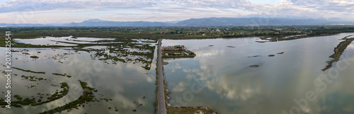 Foto Aerial panorama looking down at an asphalt roadway dividing the mirror-like marshlands and channels of Patok Lagoon, with mountains visible on the horizon in Albania
