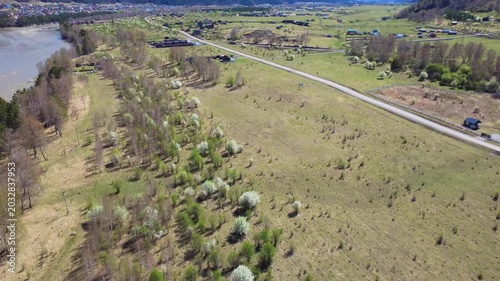 Riverbank Road Flanked By Budding Wetland Trees And Grassy Floodplain, Slow Water Curve With Roadside Lane, Spring Growth And Open Pasture, Aerial View Shows Human Access And Natural Margin