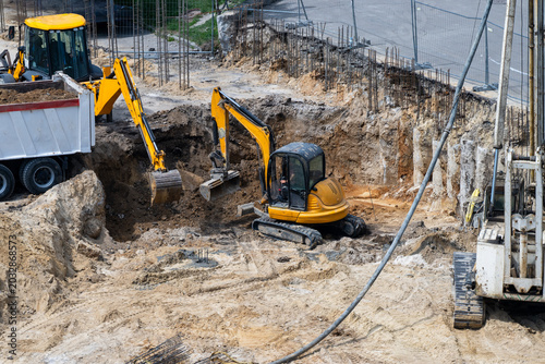 Cuadro en lienzo an active construction site where yellow excavators are digging a deep foundation pit and loading dirt into a dump truck