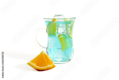 On a white background there is a glass with a handle and a blue cocktail with ice and orange.