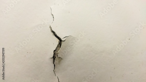 Photos Detailed view of a long crack across a textured white surface with concrete dist