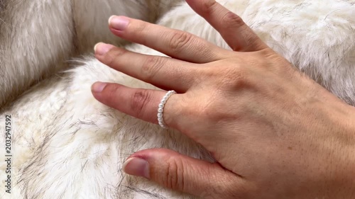Close-up of a hand wearing a delicate white ring gently touching a soft, textured fur surface, showcasing the intricate details of the ring and the luxurious background material
