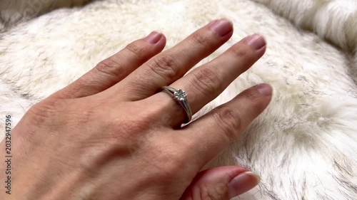 Close-up view of a hand adorned with a diamond ring placed on soft white fur, highlighting the ring's design and the luxurious texture of the fur in the background