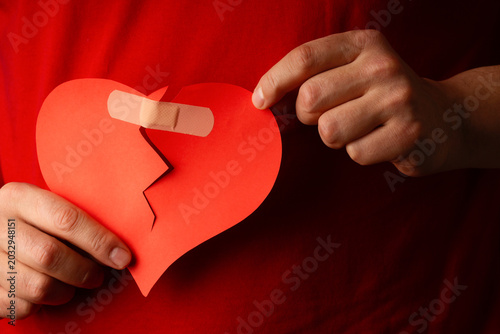 Man holding broken paper heart fixed with adhesive bandage, concept of relationship healing, psychology and heartbreak