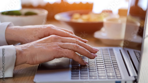 Elderly Caucasian Businesswoman Typing Laptop Lunch, Hands On Keyboard Beside Ceramic Coffee Cup And Pastry, Warm Morning Light, Blazer Sleeve And Simple Ring, Neat Manicure, Smartphone And Notebook