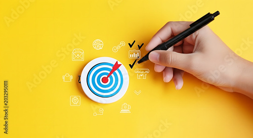 Hand drawing bullseye target on sticky note with black marker on yellow background