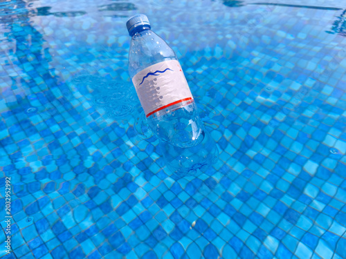 Close-up of a plastic water bottle submerged in a swimming pool with blue mosaic tiles and clear water.