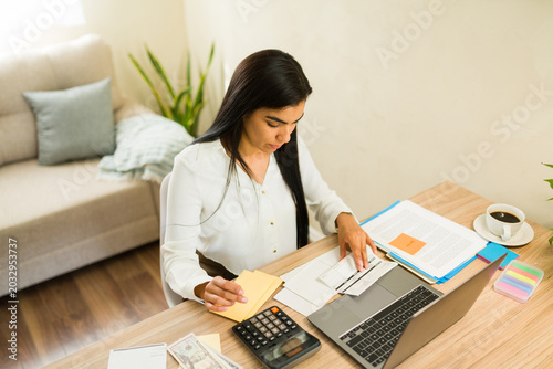 Latin woman managing personal finance and budgeting money on a laptop, calculating expenses for taxes and economic planning
