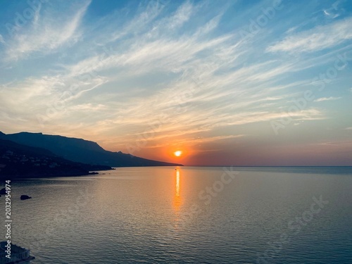 Sunset over calm sea with mountain coastline — golden reflection on water