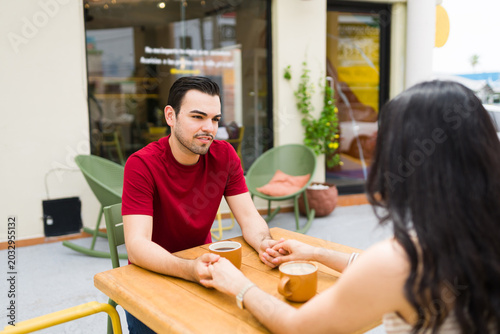 Hispanic couple holding hands on a casual date at an outdoor cafe, enjoying coffee and conversation, sharing a romantic moment