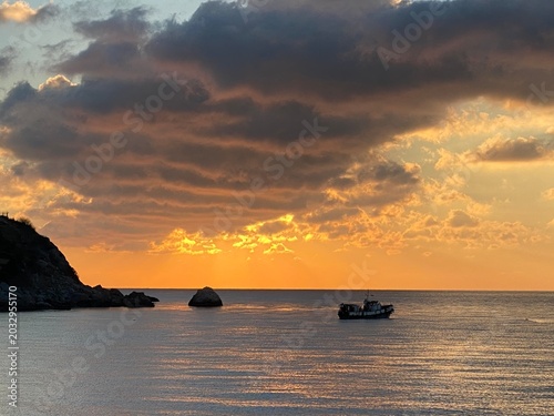 Fishing boat on calm sea at golden sunset — dramatic clouds and sun rays