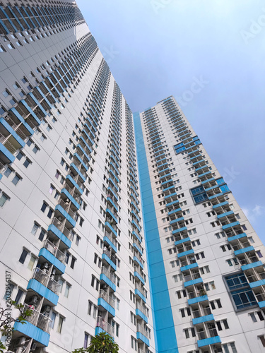Low-angle view of a tall, modern apartment building with white and blue exterior against a blue sky.