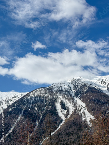Majestic snow-capped Altai Mountains under a bright blue sky with clouds in Xinjiang, China.