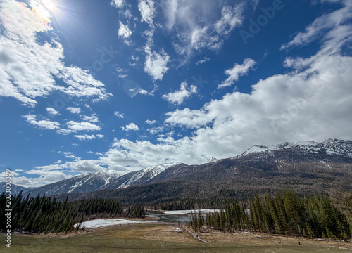 Majestic snow-capped Altai Mountains under a bright blue sky with clouds in Xinjiang, China.