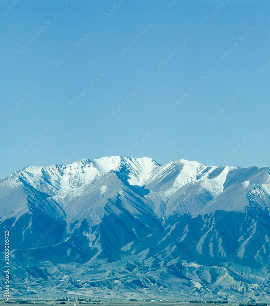 Fototapeta premium Majestic snow-capped Altai Mountains under a bright blue sky with clouds in Xinjiang, China.