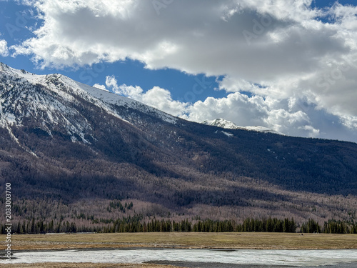 Majestic snow-capped Altai Mountains under a bright blue sky with clouds in Xinjiang, China.