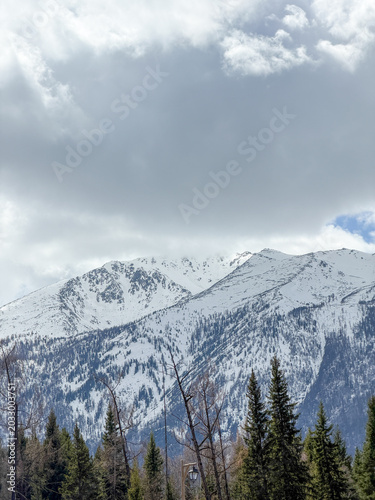 Majestic snow-capped Altai Mountains under a bright blue sky with clouds in Xinjiang, China.