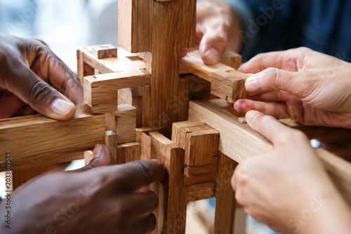 Diverse hands building a wooden toy structure together