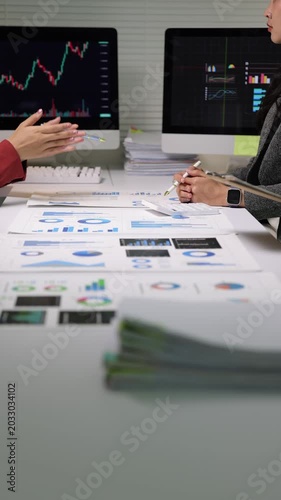 Financial analysts discussing stock market data in a meeting, analyzing financial charts and stock market data on documents and computer screens.