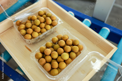 Fotografia Fresh sweet tropical longan fruit inside clear plastic packaging resting on wood
