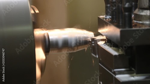 Video pan shot of a CNC lathe machine rough cutting a metal cone-shaped part with a liquid coolant method.