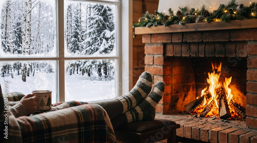 Person wearing warm wool socks relaxing with a hot mug while sitting by a cozy fire during the winter season