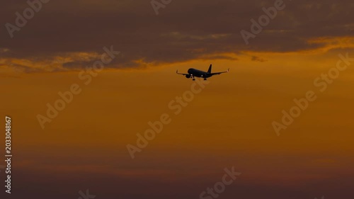 Cinematic silhouette of a commercial passenger airplane with landing gear deployed, flying against a dramatic and vibrant orange sunset sky. Beautiful atmospheric background for travel concepts.