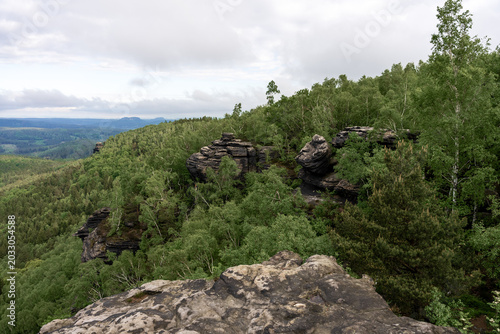 Dramatic morning view from Grosser Zschirnstein, Saxon Switzerland, Germany, with distant horizon, layered clouds, deep forest below and sandstone rocks in foreground.
